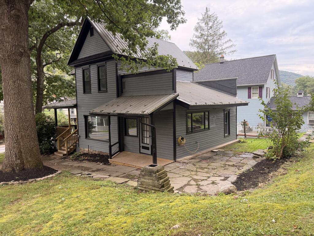 Charcoal-gray two-story house with a steep metal roof, covered entry, and stone-paved yard.