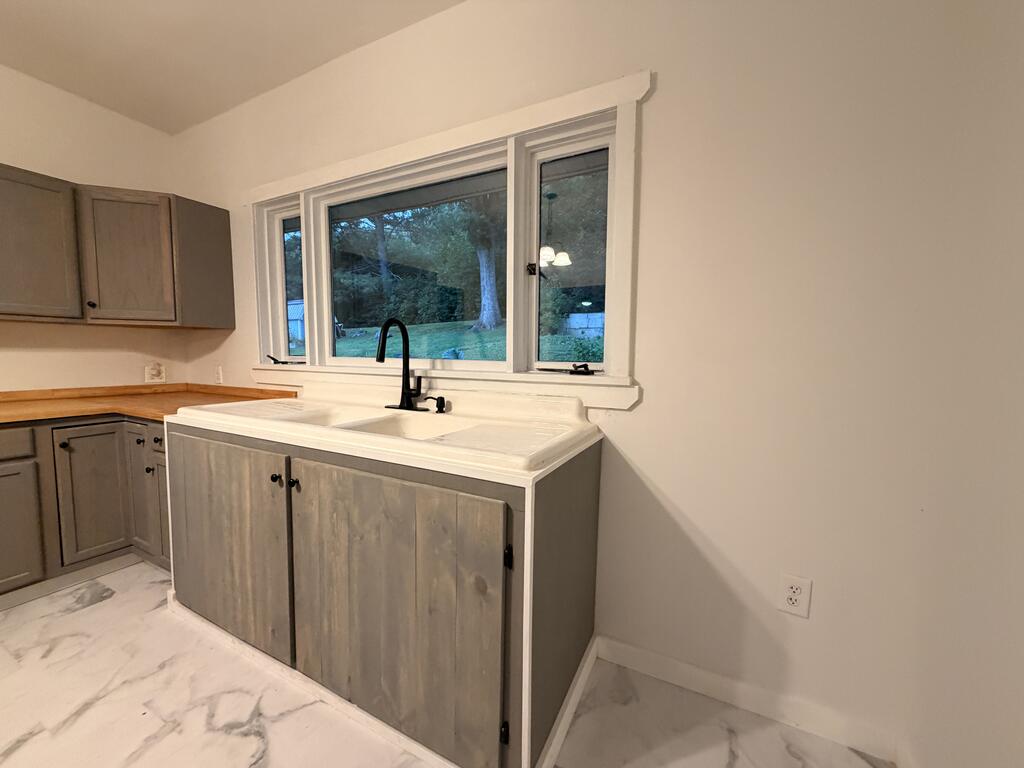 Kitchen sink beneath a wide window, with gray cabinets and a view of the yard.