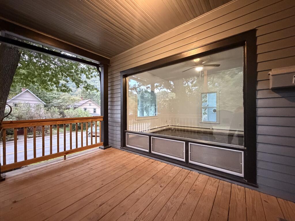 Covered porch with wood decking and railing, large picture window, and views toward a tree-lined street.