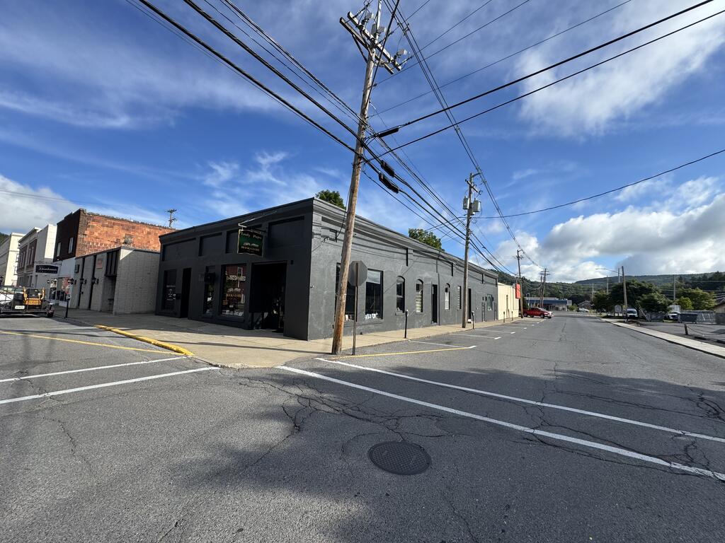 Dark gray commercial corner building with storefront entrances and a long row of narrow windows.