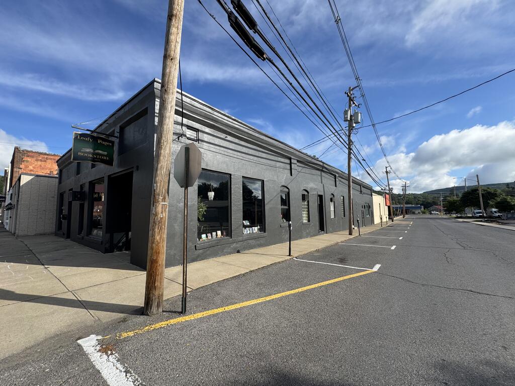 Dark-gray commercial storefront with large windows and a Leafy Pages Bookstore sign beside angled parking.