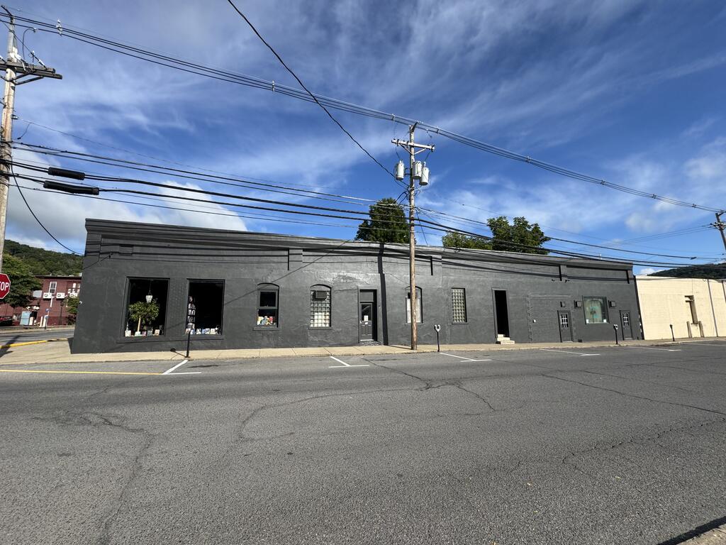 Long, dark gray commercial building with storefront windows and angled street parking.