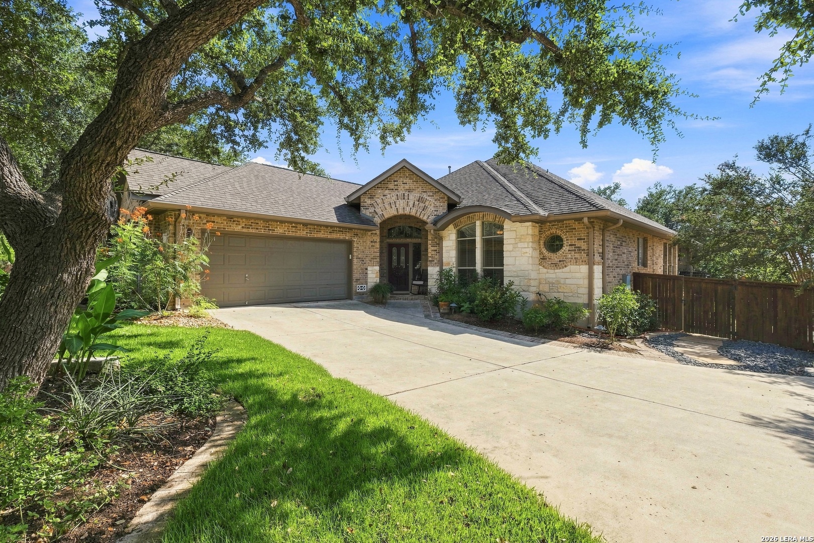 Single-story brick and stone house with an arched entry and broad driveway beneath a mature tree.