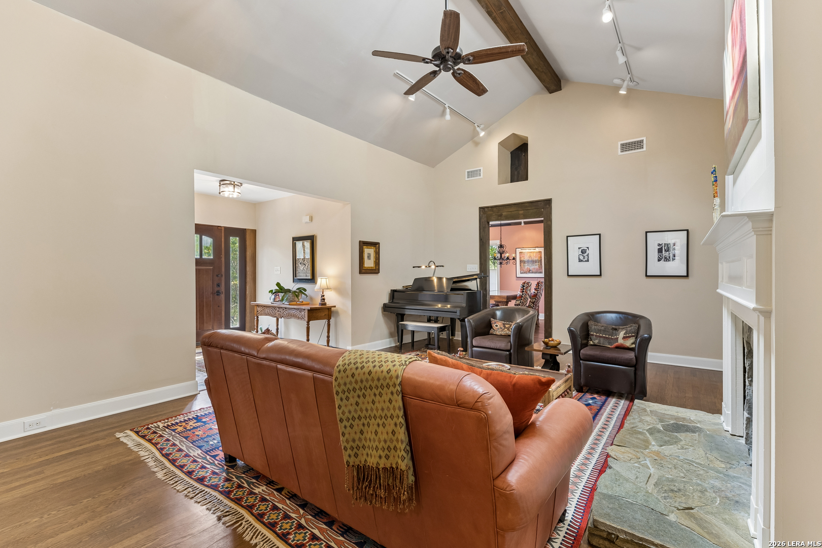 Furnished living room with vaulted ceiling, exposed beam, grand piano, and stone fireplace.