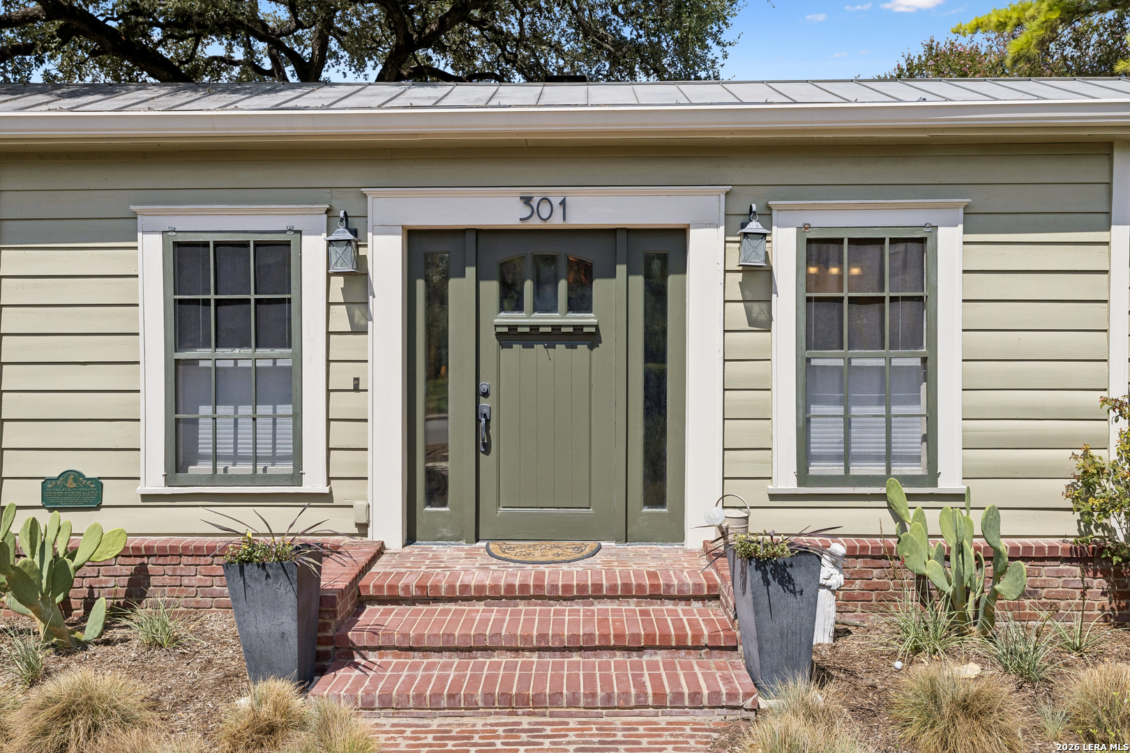 Home entrance with a dark green door, brick steps, and potted plants.