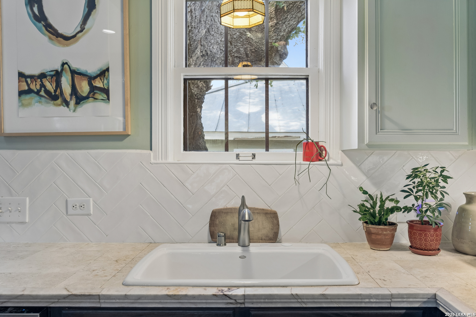 Kitchen sink beneath a window, set in a stone counter with white herringbone tile backsplash.