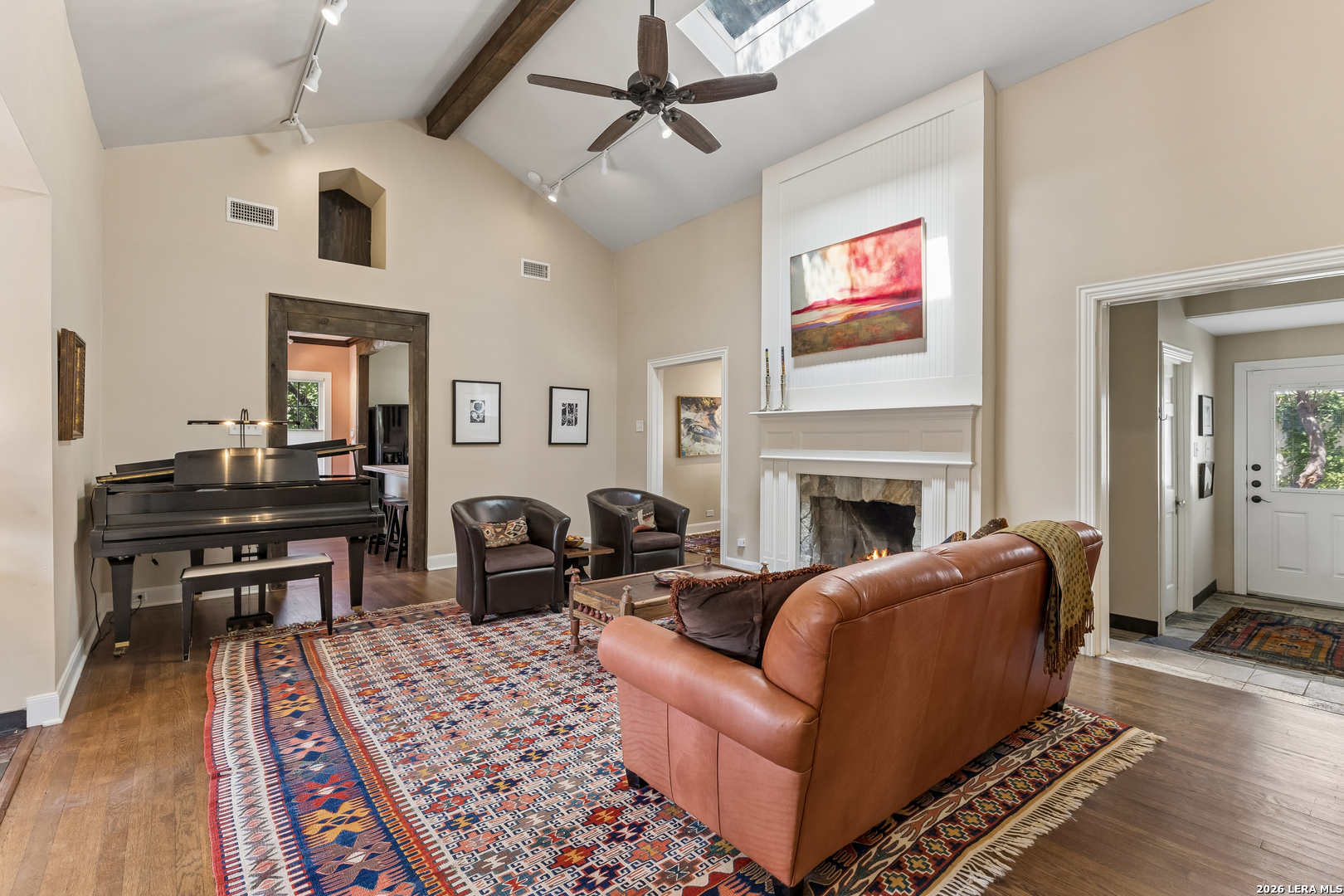 Vaulted living room with a fireplace, grand piano, leather sofa, and colorful patterned rug.
