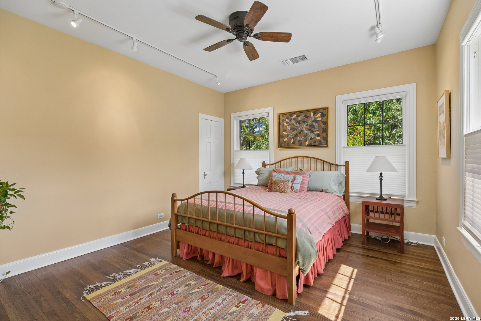 Bedroom with a wooden bed, pink bedding, two windows, and hardwood floors.