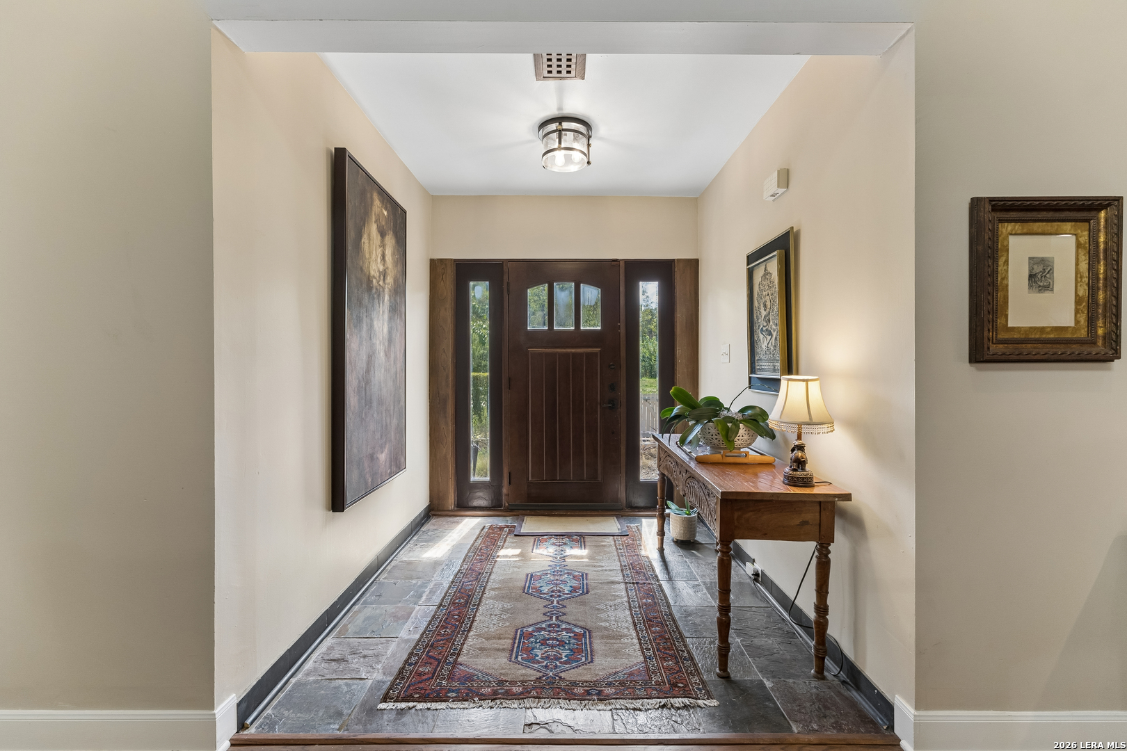 Entry foyer with a dark wood front door, slate flooring, patterned runner, and wooden console table.