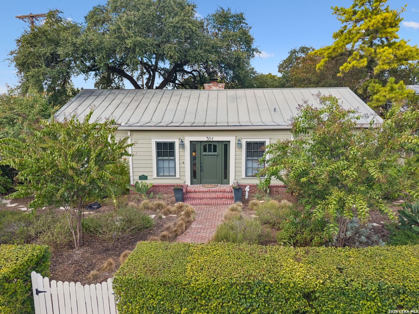 Home with a green front door, metal roof, and brick walkway through a landscaped garden.