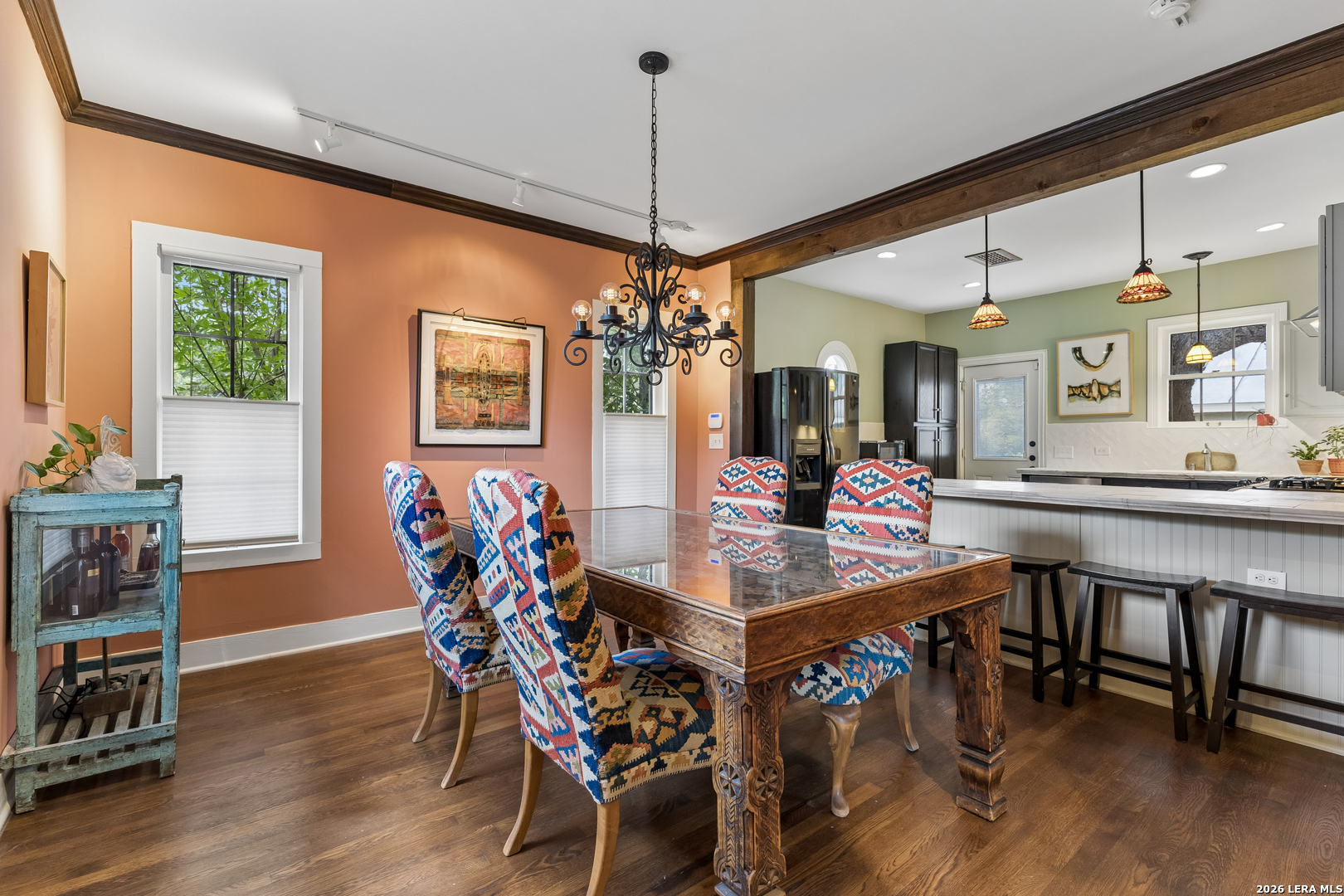 Dining room with a carved wood table and colorful chairs beside an open kitchen.