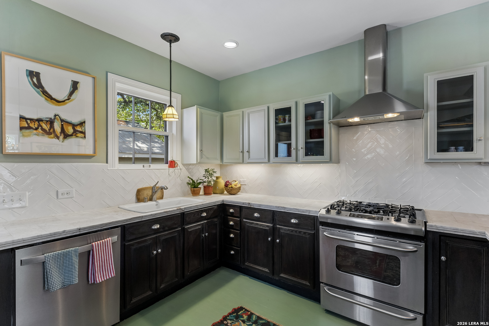 Kitchen with dark cabinets, white herringbone backsplash, stainless range, and a window above the sink.
