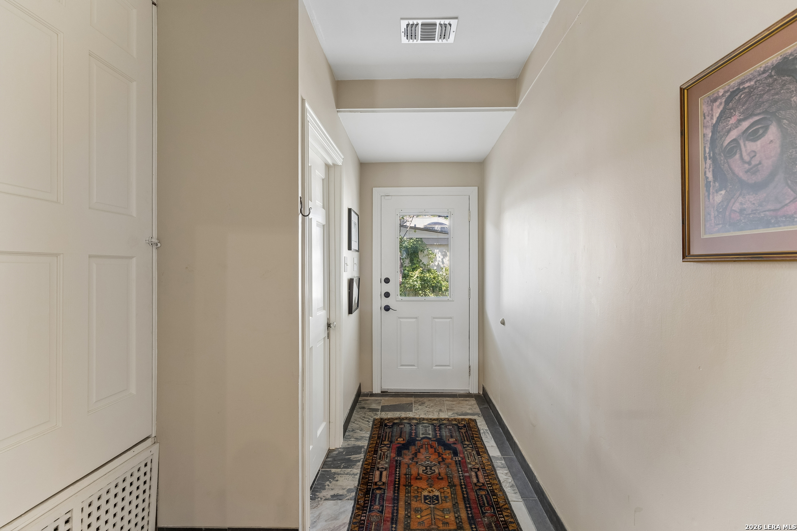 Entry hallway with tiled floor, patterned runner, framed art, and a white door with a window.