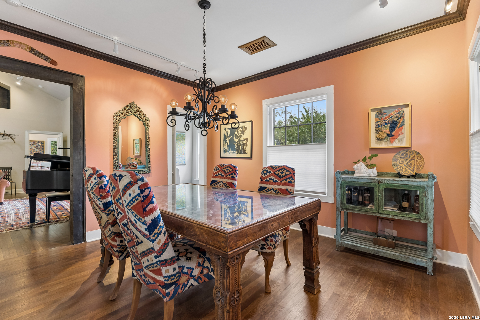 Dining room with peach walls, patterned chairs, a carved glass-top table, and an ornate chandelier.