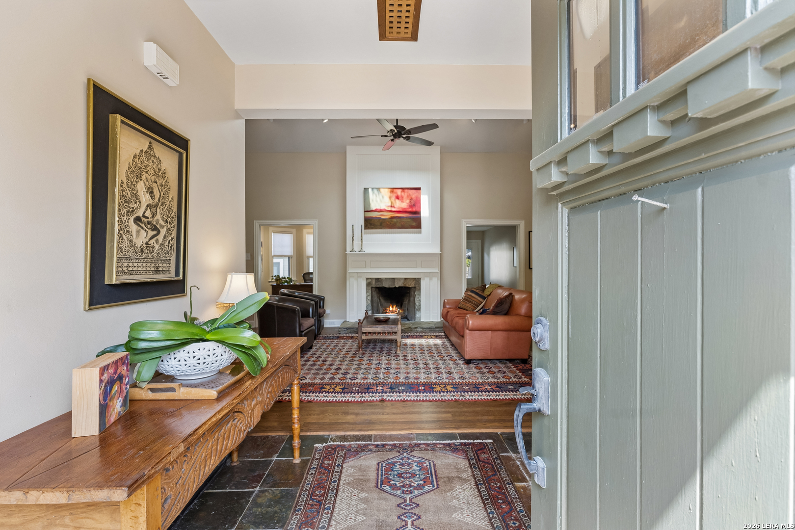 Living room with a white fireplace, leather seating, patterned rugs, and an open green front door.