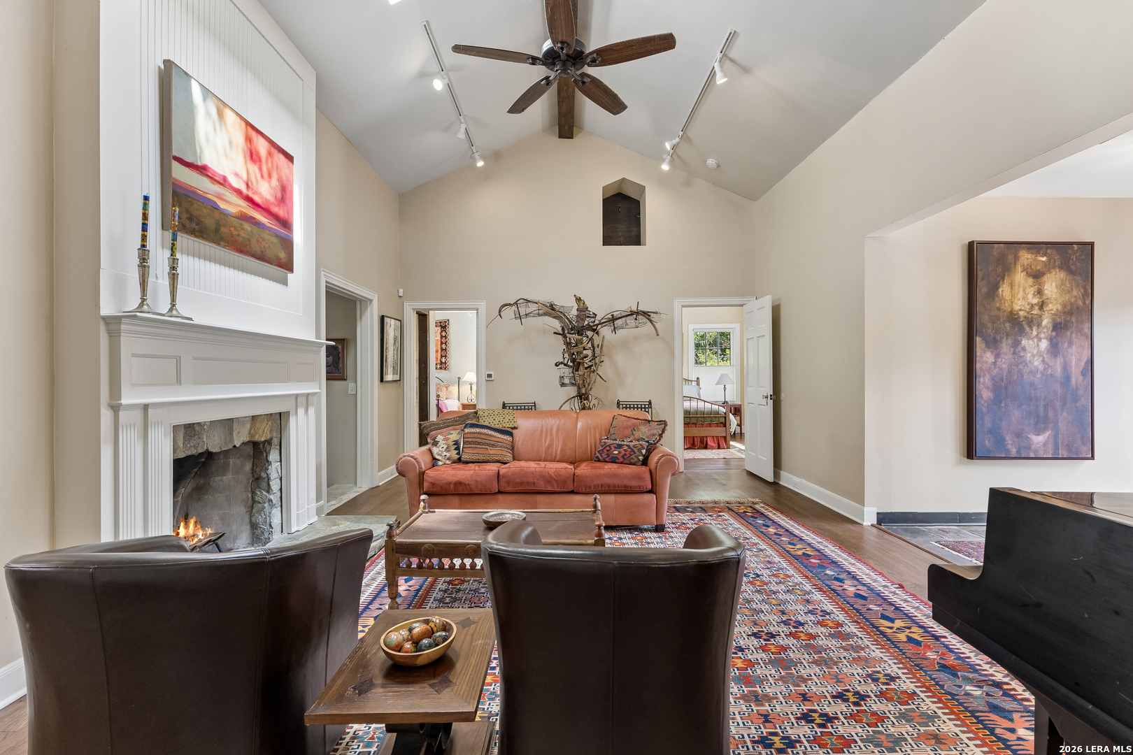 Living room with a vaulted ceiling, white fireplace, leather seating, and a colorful patterned rug.