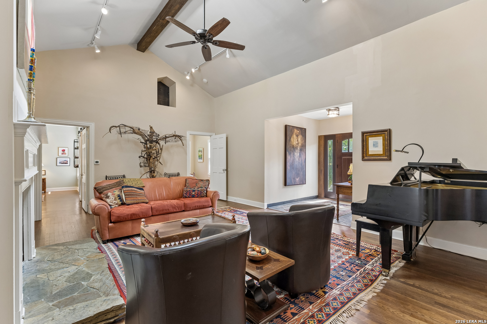 Living room with vaulted ceiling, leather seating, colorful rug, and black grand piano.