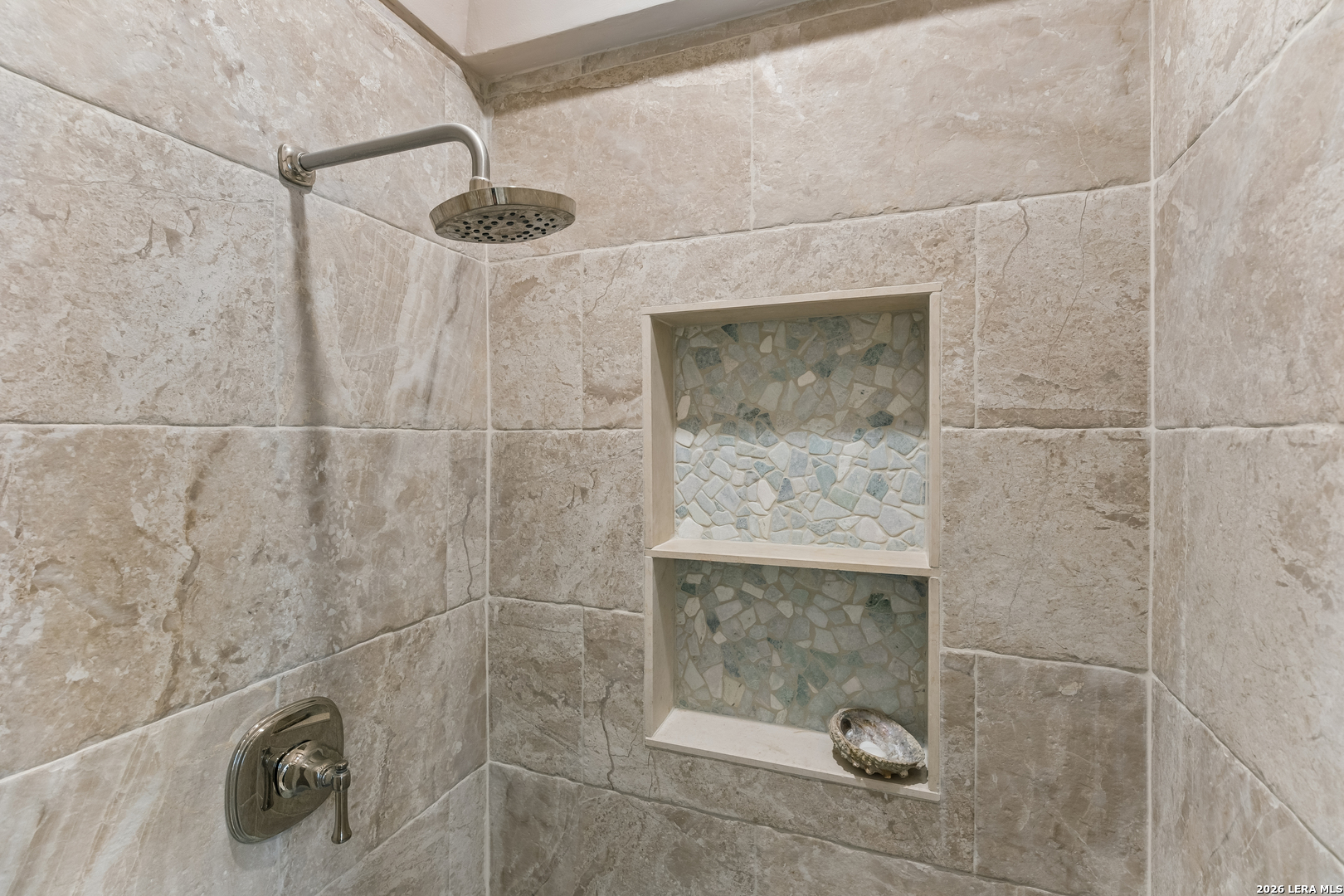 Tiled shower with a rain showerhead and two recessed mosaic niches.