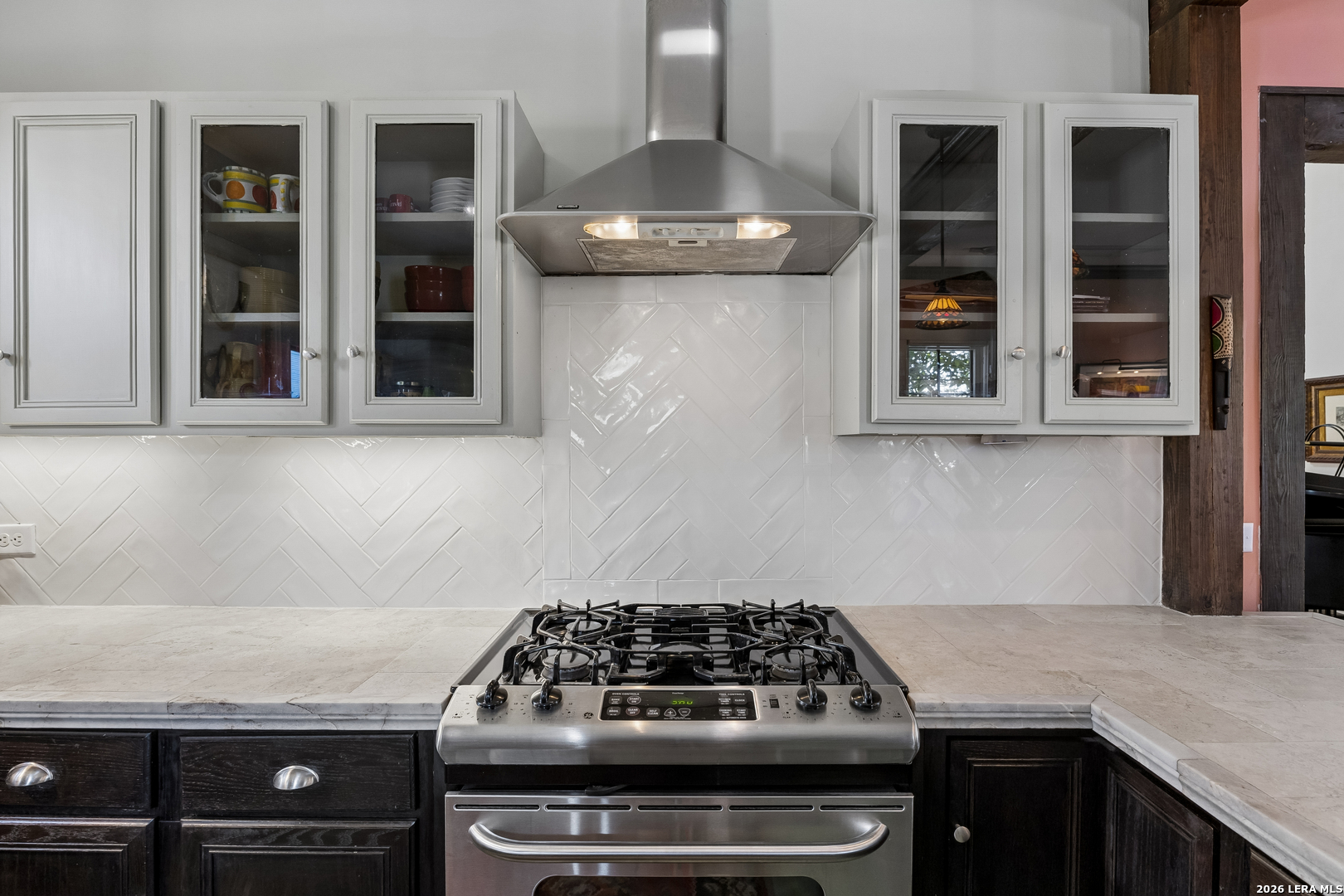 Kitchen with a stainless gas range, glass-front cabinets, and white herringbone tile backsplash.