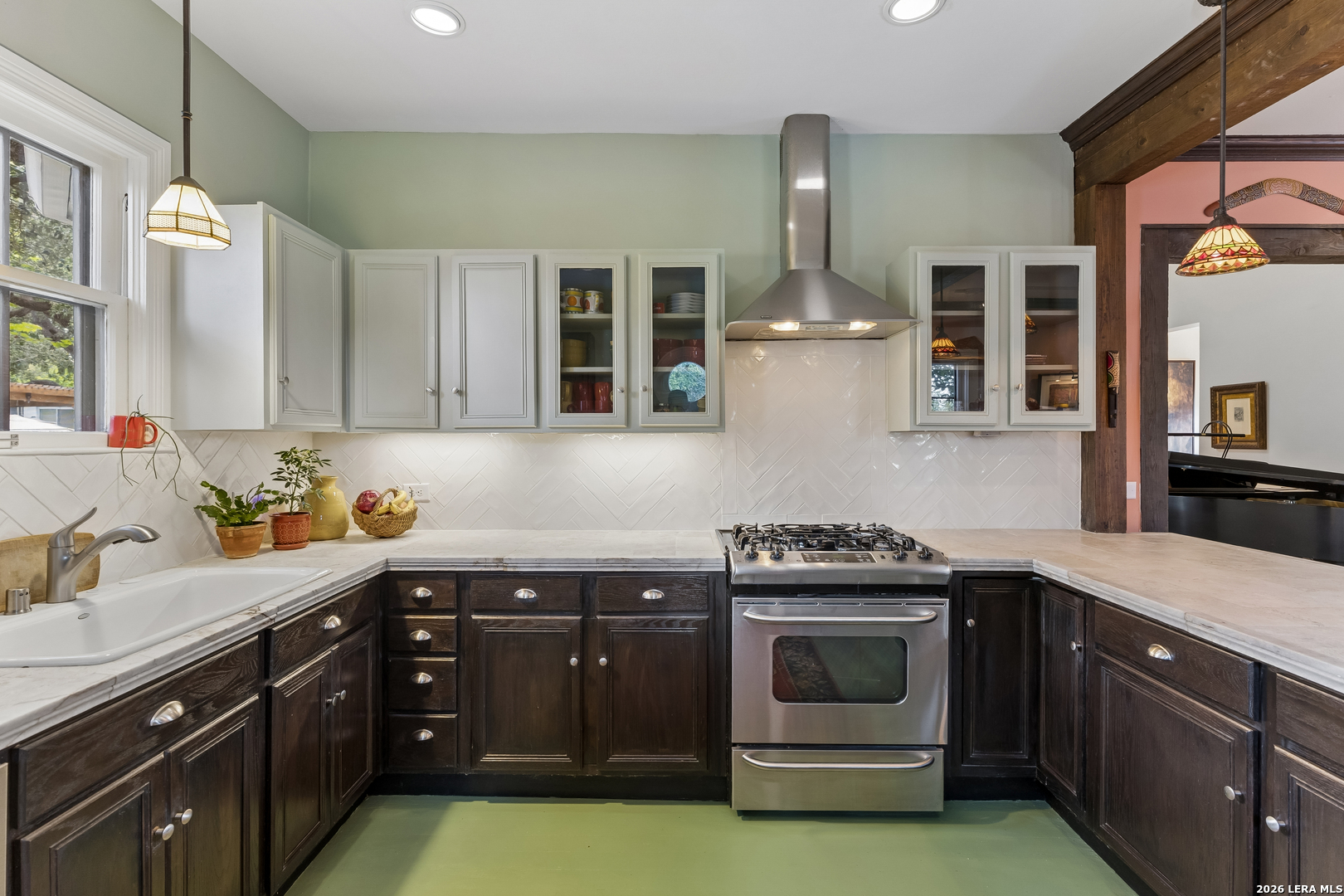 Kitchen with dark wood cabinets, marble counters, white tile backsplash, and stainless steel range.