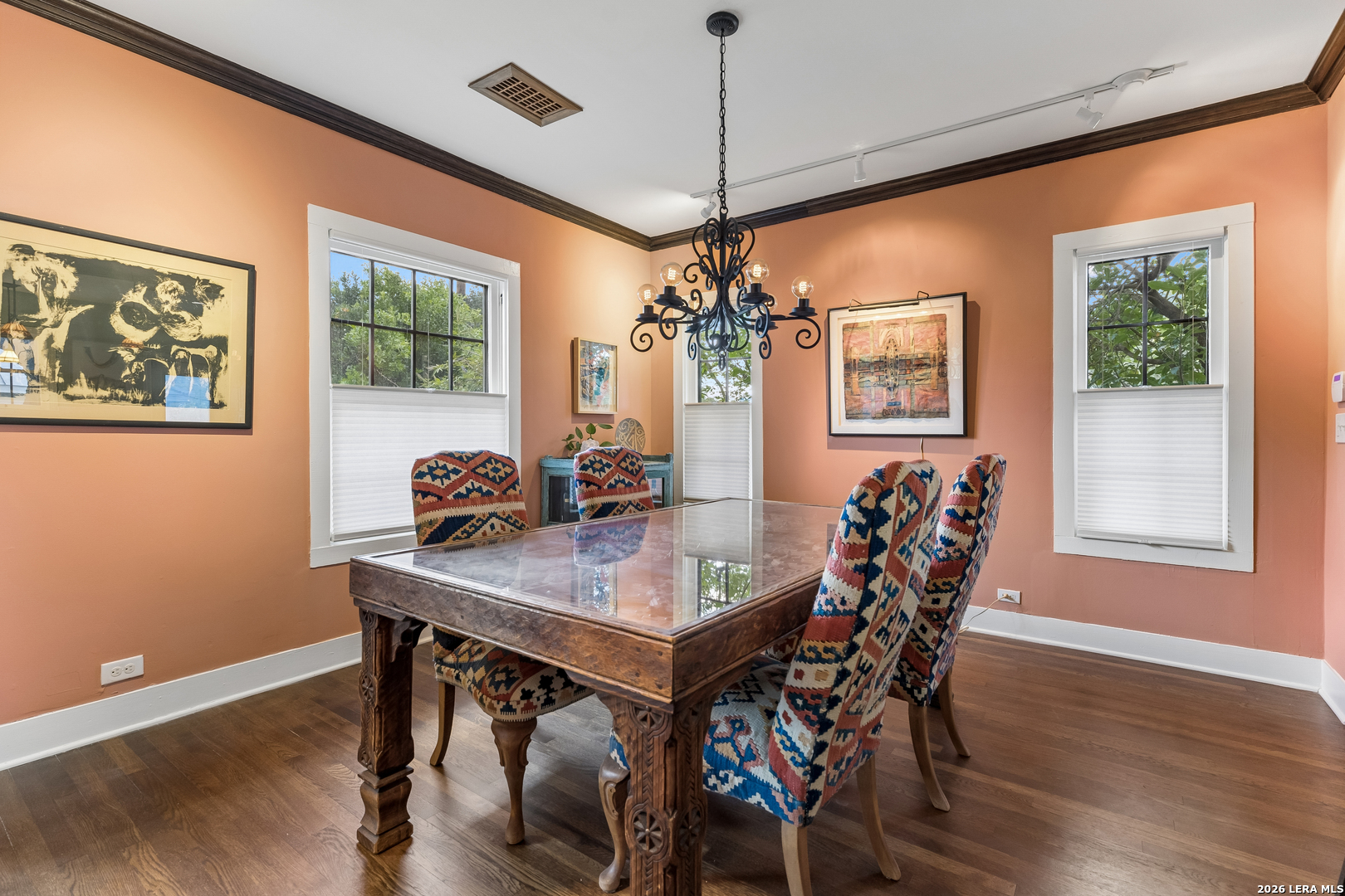 Dining room with peach walls, a glass-topped wood table, patterned chairs, and a wrought-iron chandelier.