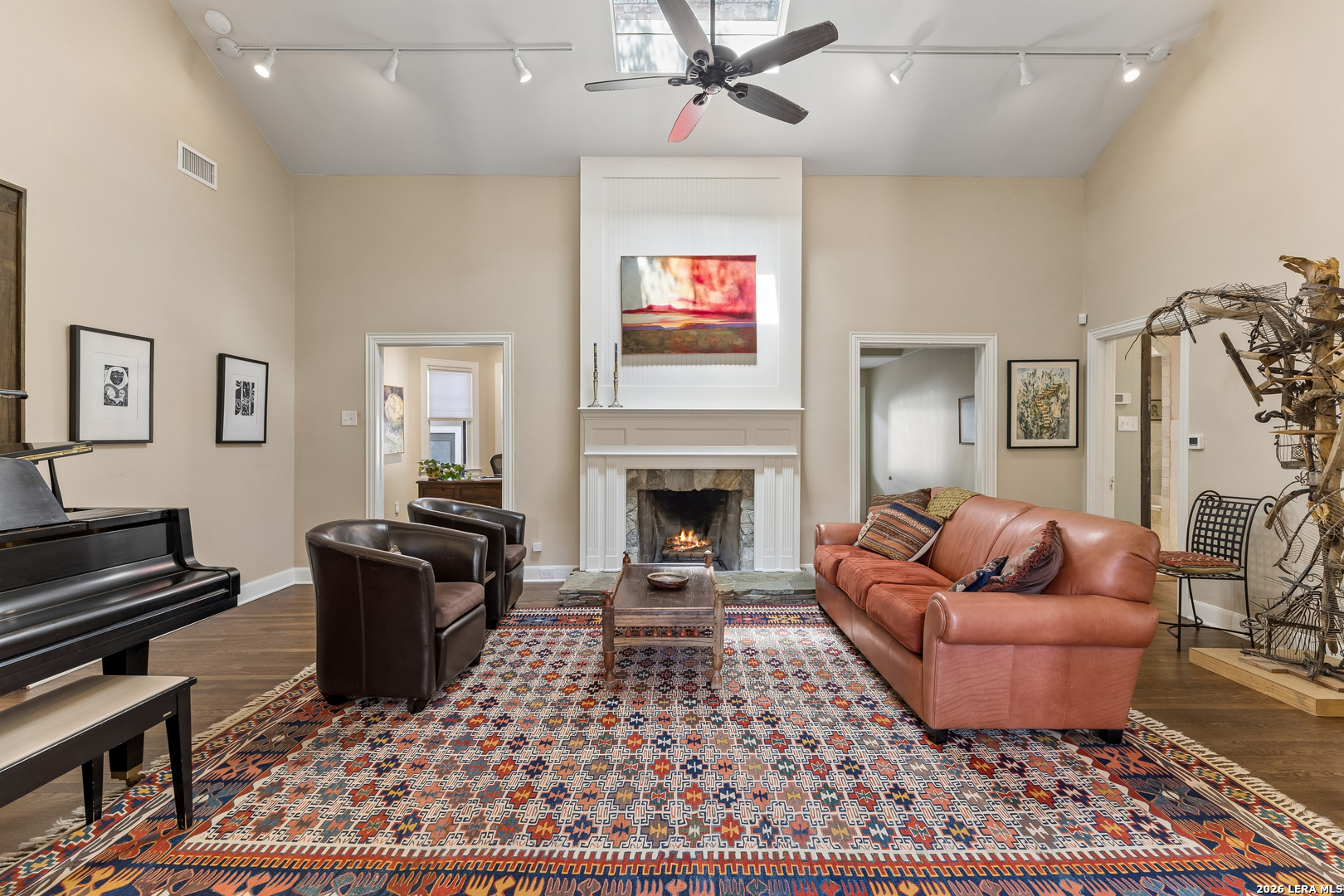 Living room with a lit fireplace, leather seating, grand piano, and colorful patterned rug.