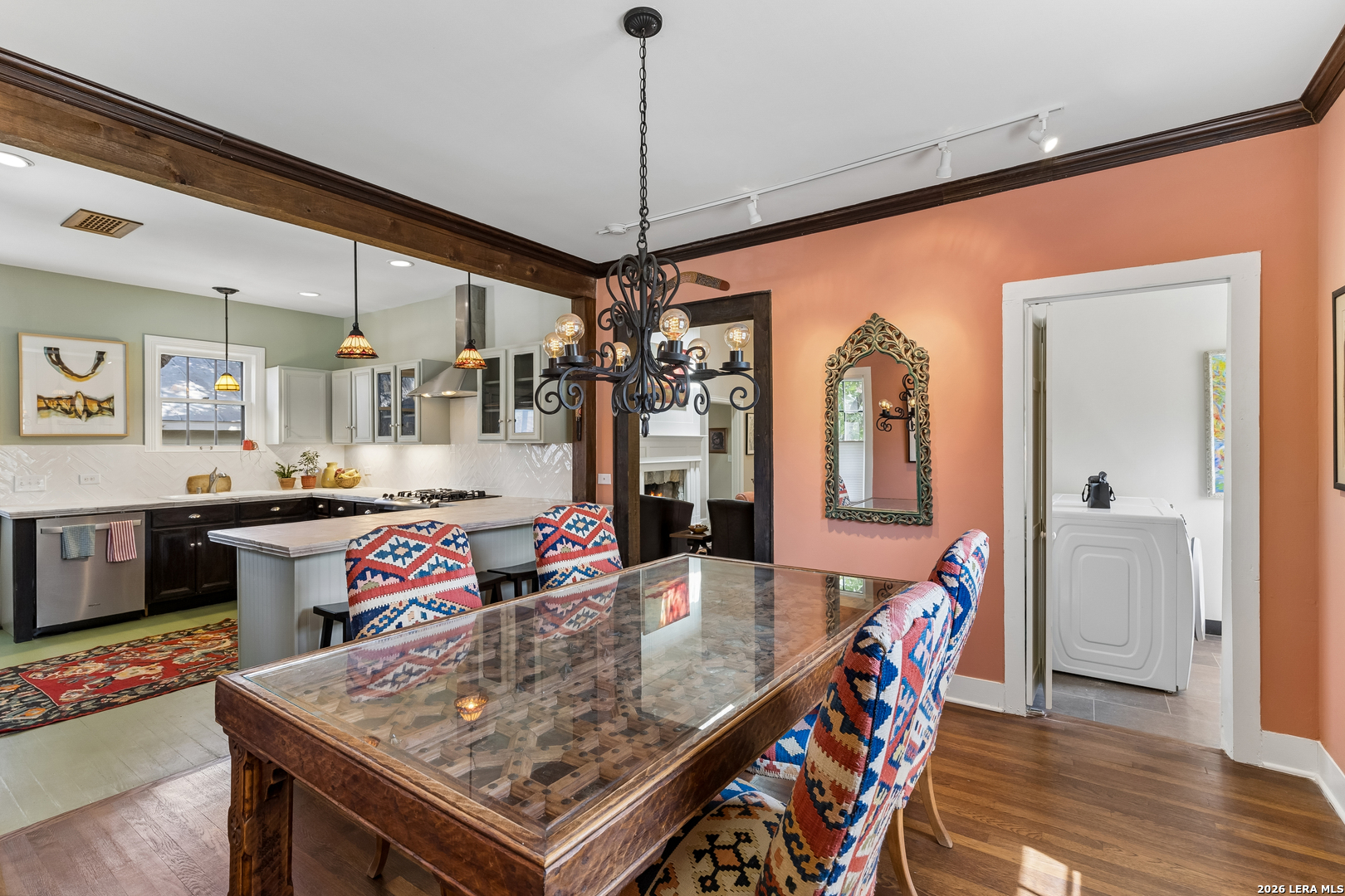 Dining room with glass-top wooden table and patterned chairs, opening onto a kitchen and laundry room.