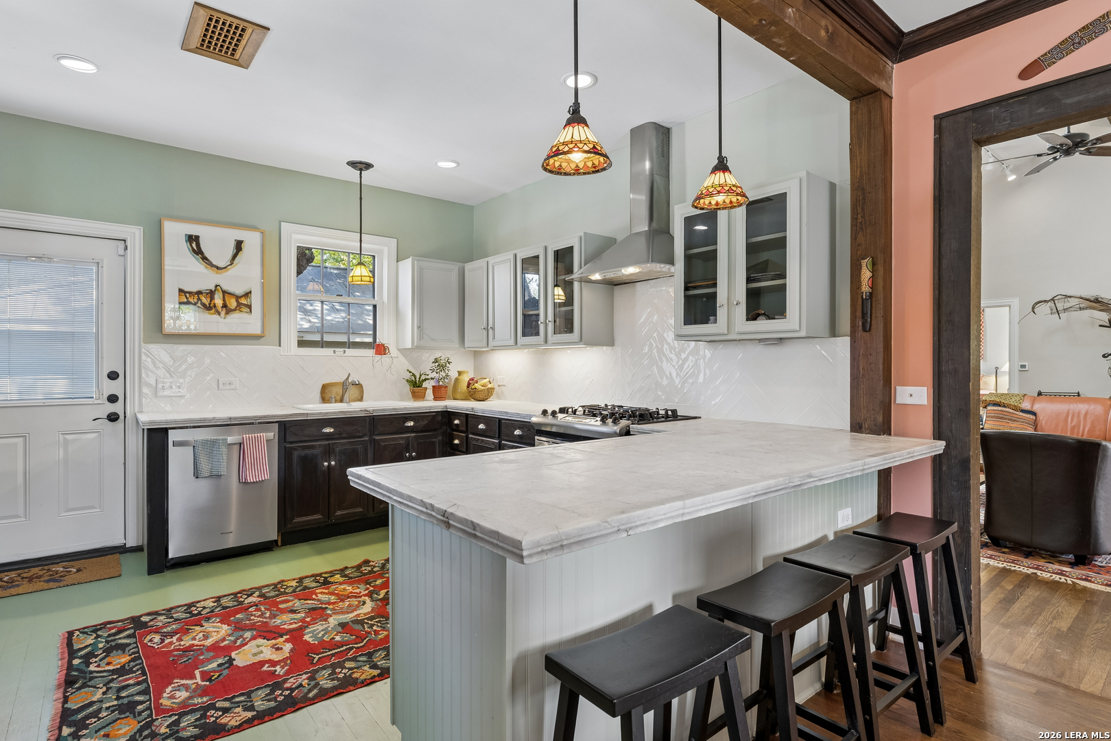 Kitchen with a large marble island, dark cabinets, stained-glass pendant lights, and a colorful patterned rug.