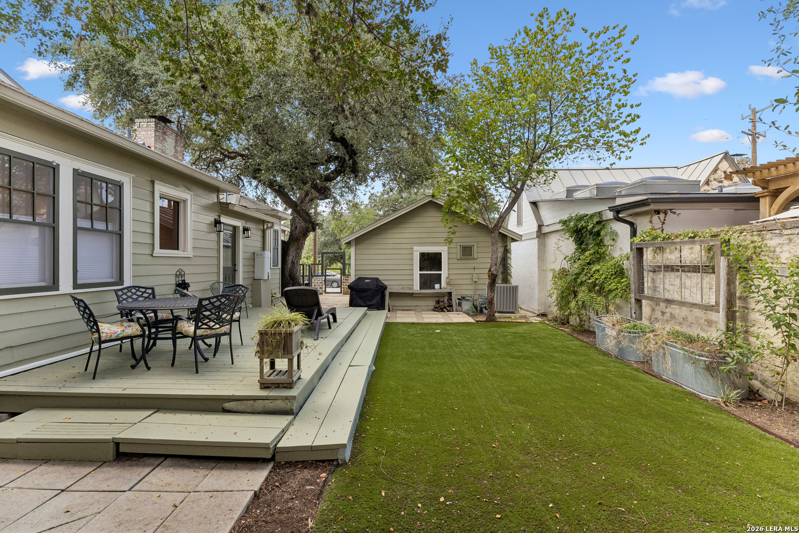 Backyard with raised dining deck, artificial turf, mature trees, and a small detached outbuilding.