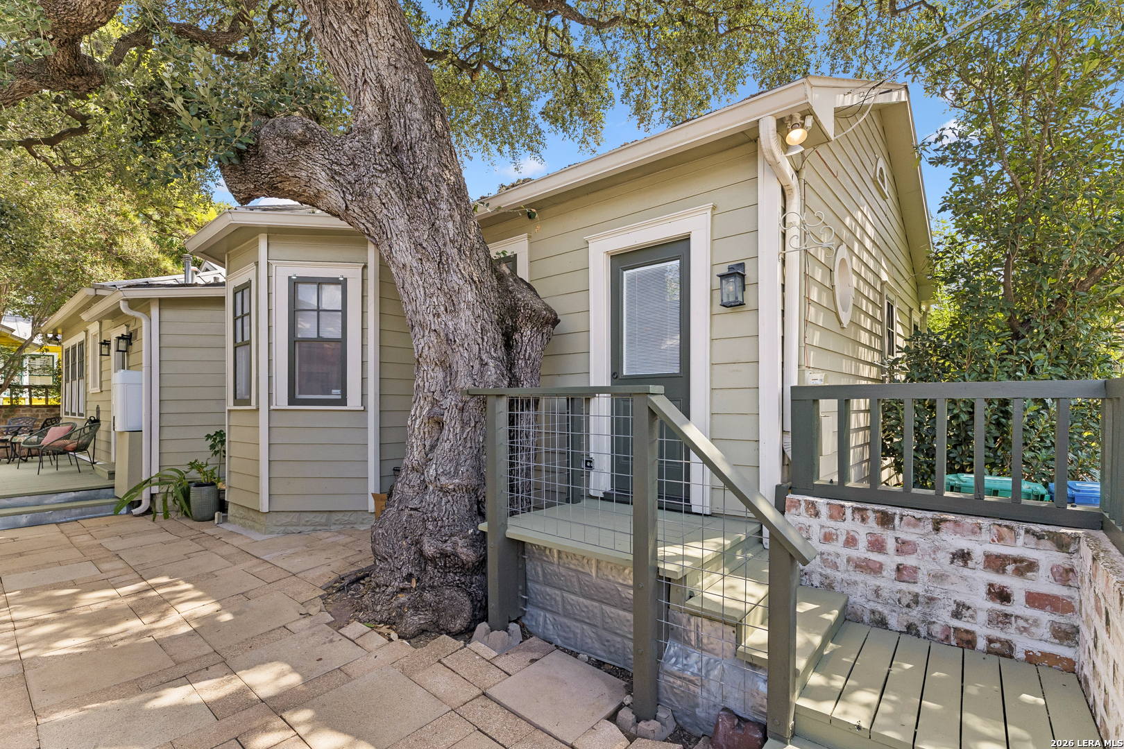 Home exterior with a raised entry deck, paved walkway, and large oak tree beside the house.