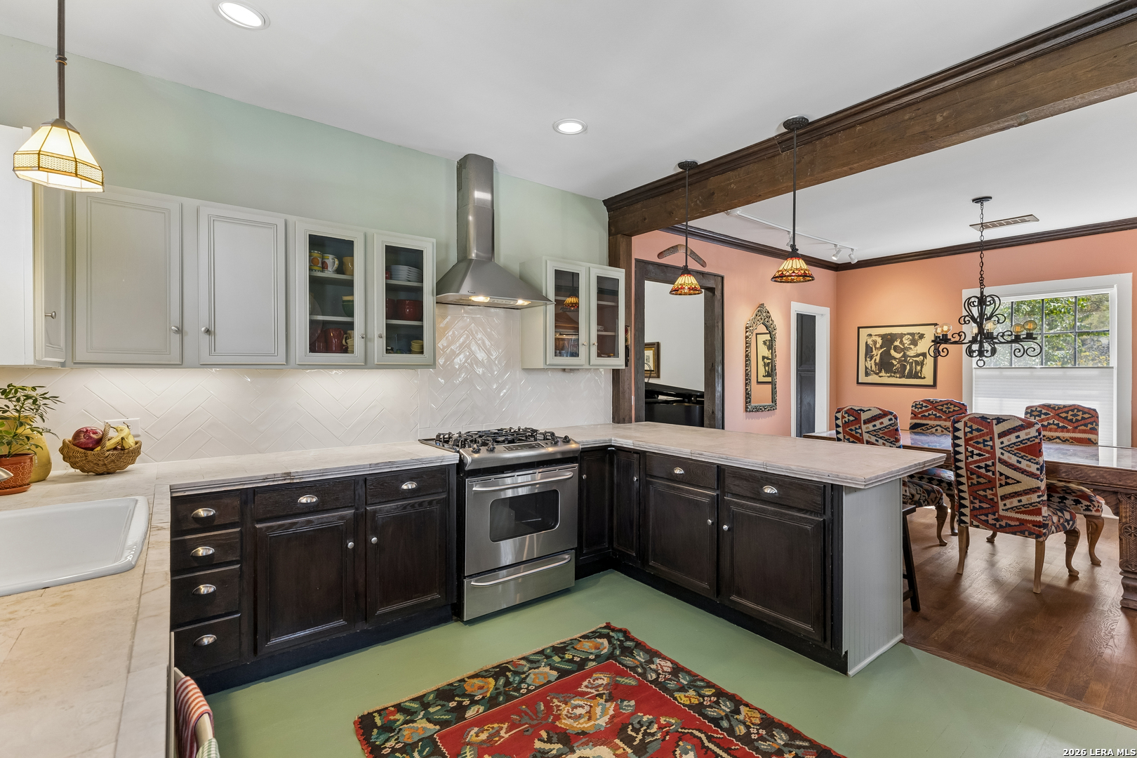 Kitchen with dark wood cabinets, stainless steel range, white tile backsplash, and adjoining dining area.