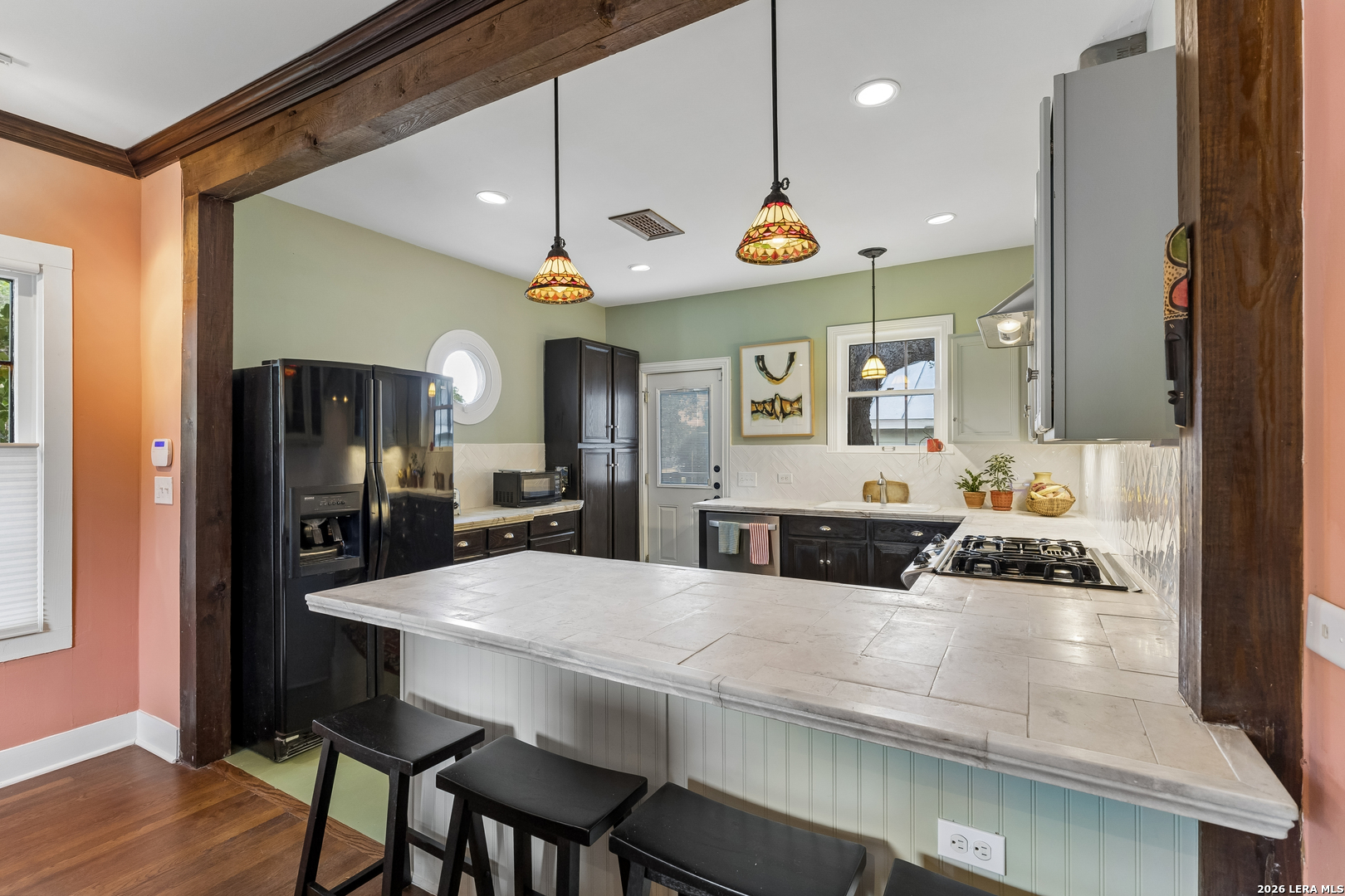 Kitchen with a large tiled island, dark cabinets, black appliances, and stained-glass pendant lights.