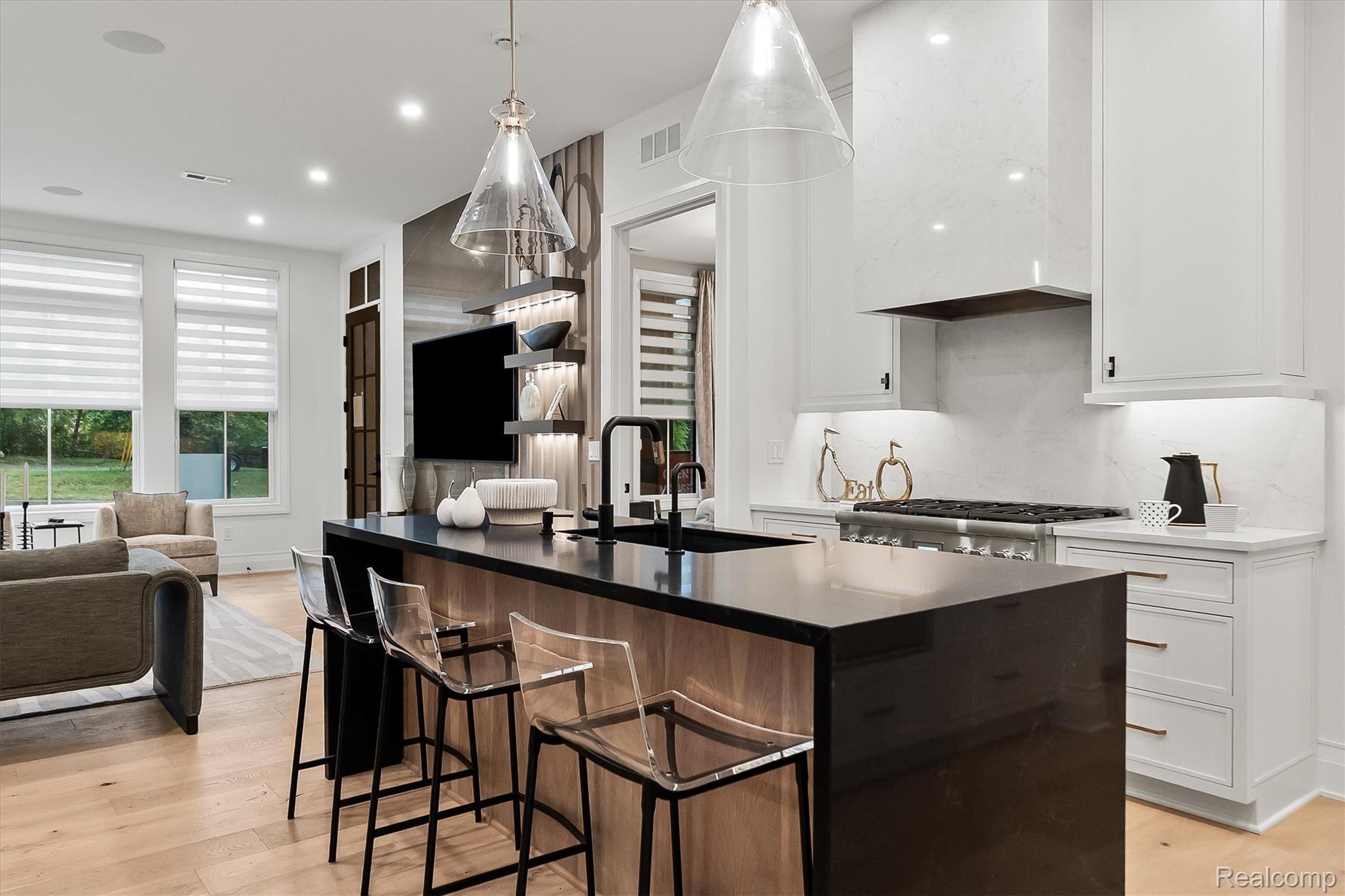 Open-plan kitchen with a large black island, white cabinetry, marble-look backsplash, and adjacent living area.