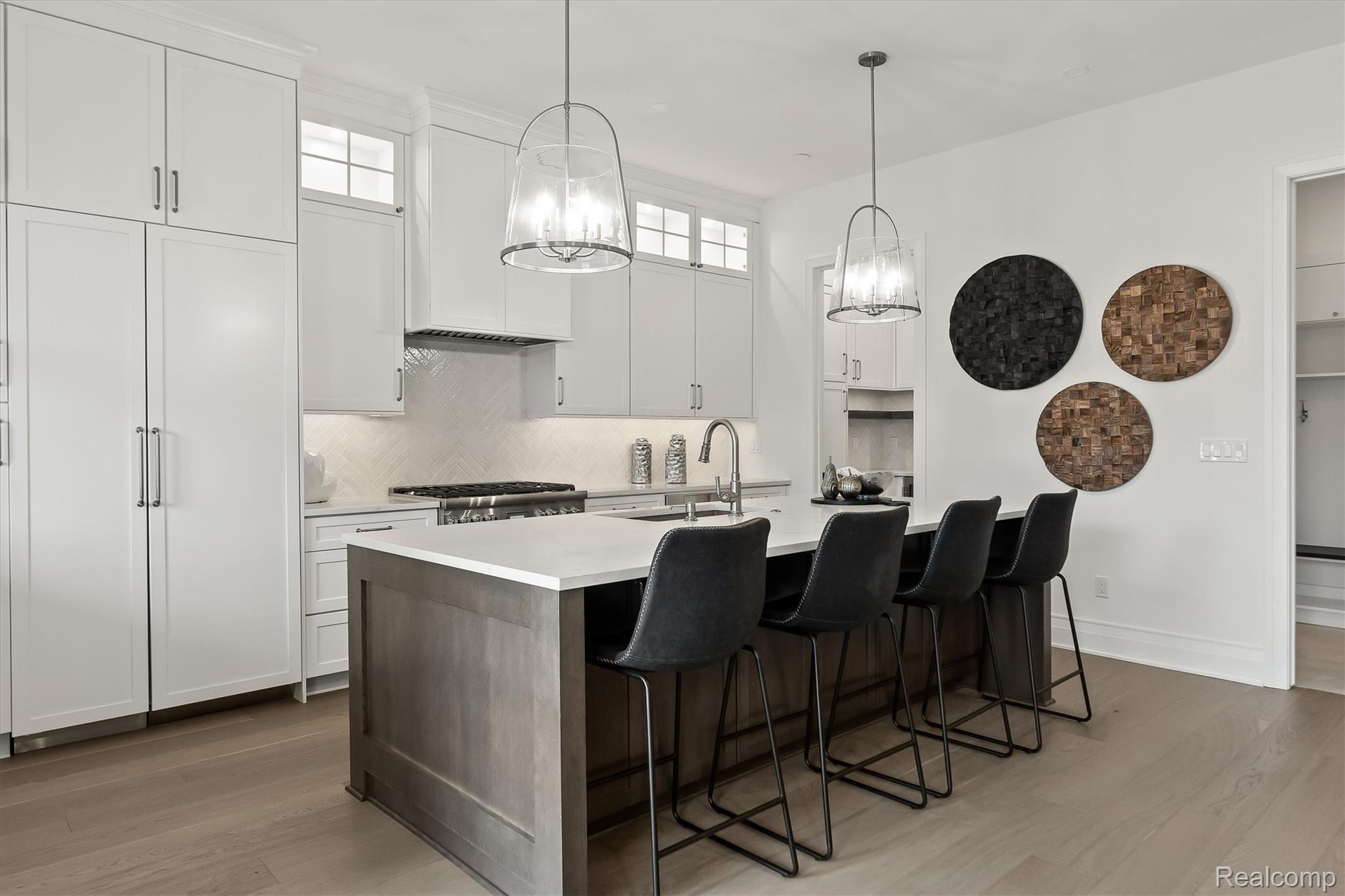 Modern kitchen with a gray island, four black stools, white cabinetry, and glass pendant lights.