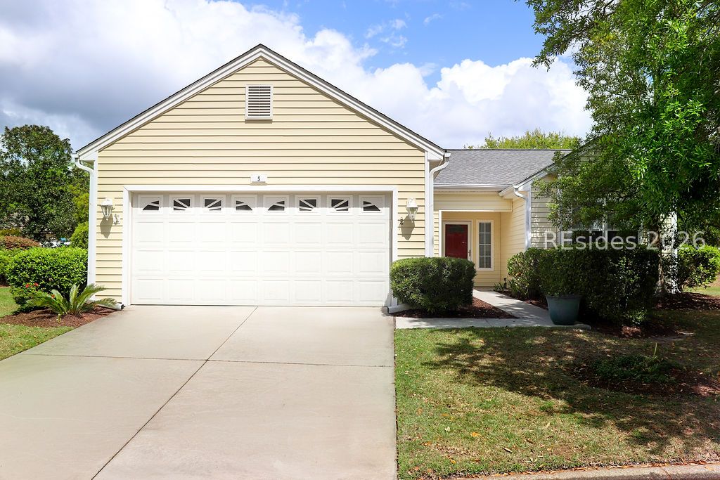 Pale yellow home with a wide white garage door, concrete driveway, and landscaped front yard.