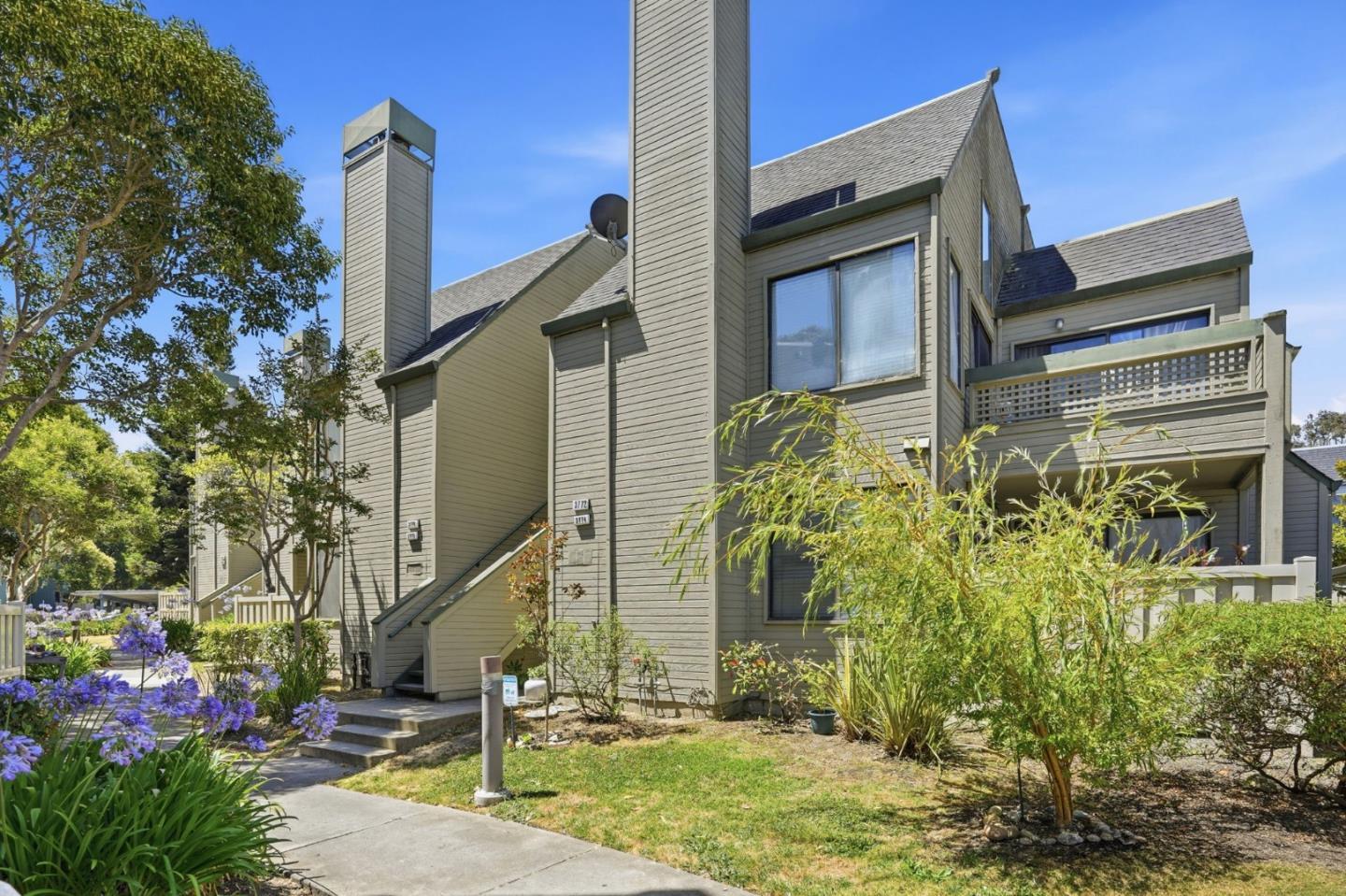 Gray multi-unit home with gabled roofs and balconies beside a landscaped walkway.