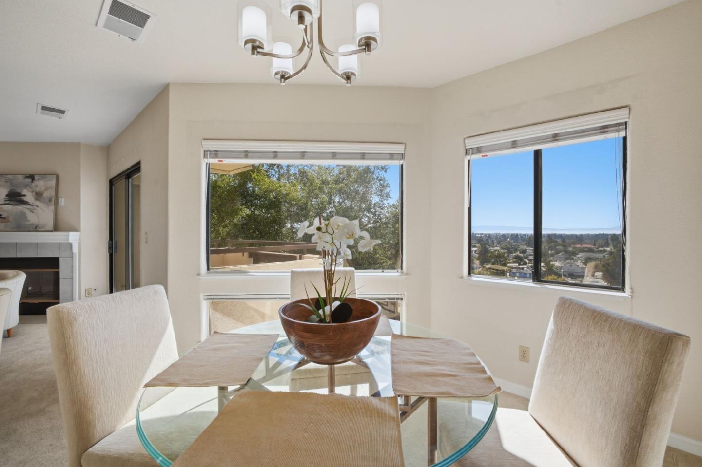 Dining area with a glass table and large windows overlooking trees and a distant residential view.