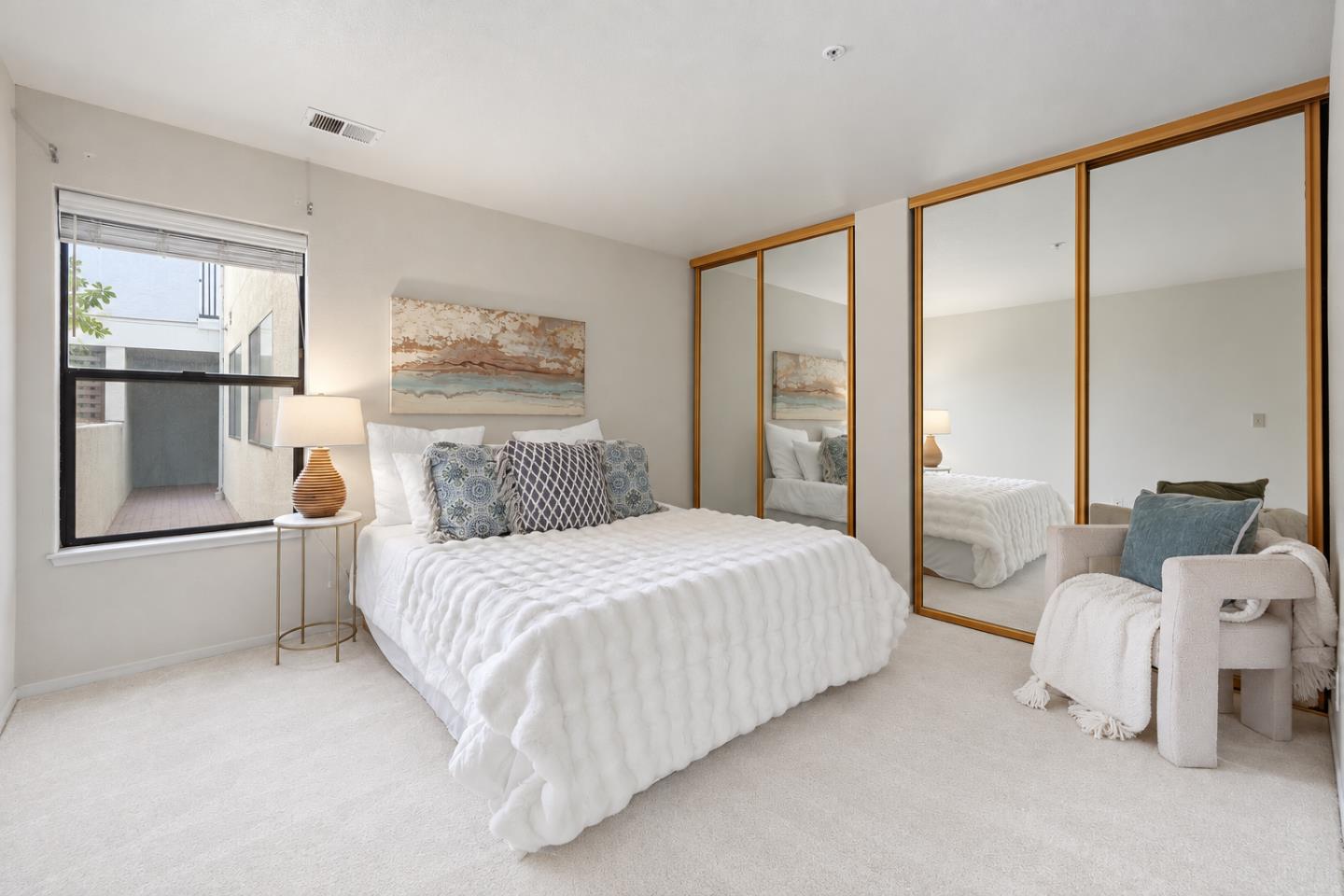 Staged bedroom with a white bed, mirrored wood-trimmed closet doors, and an armchair.