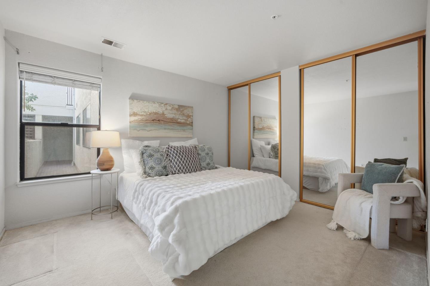 Bedroom with a white quilted bed, mirrored wood-trimmed closet doors, and a chair beside the bed.