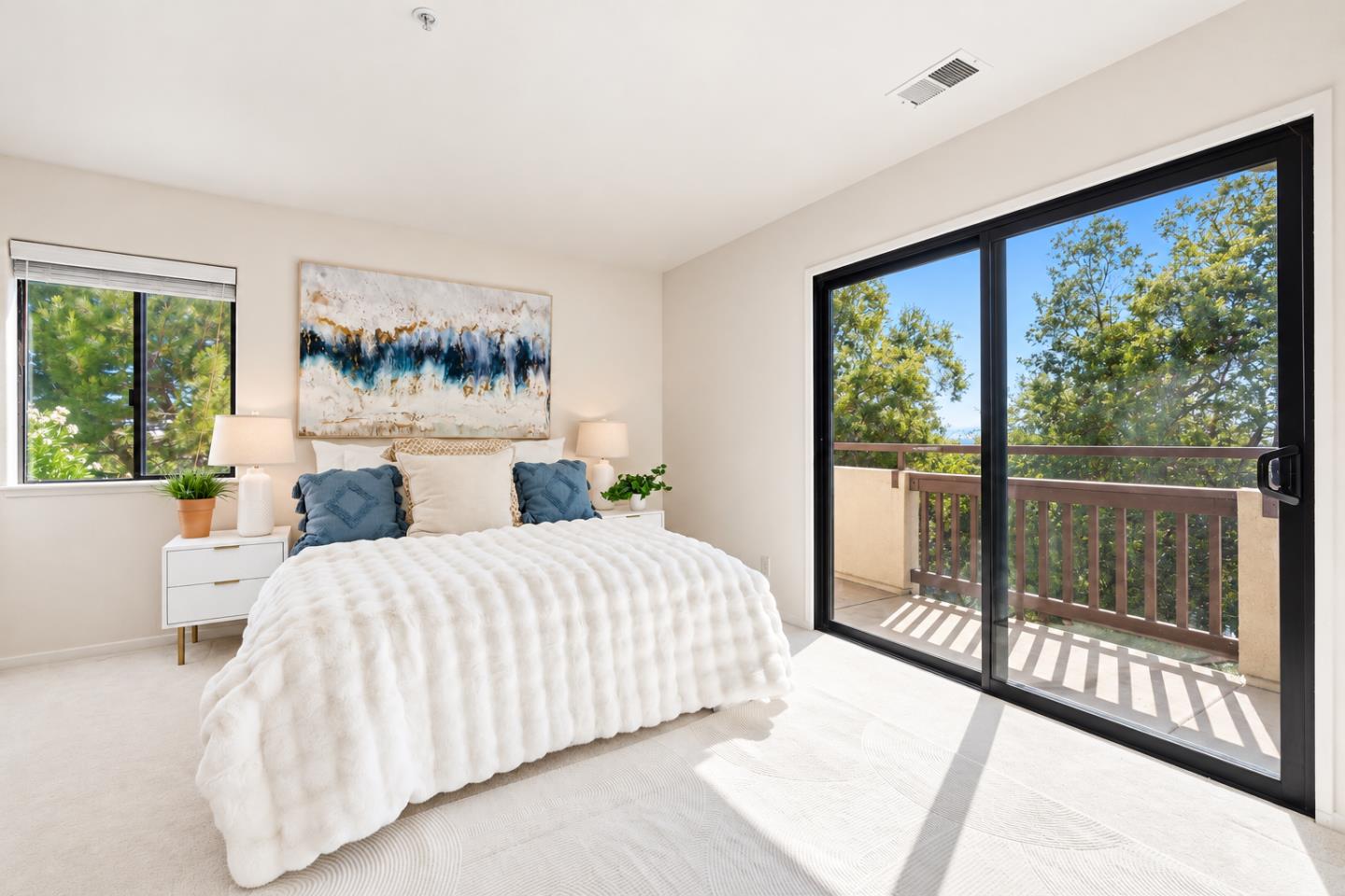 Staged bedroom with a white bed and sliding glass doors to a tree-lined balcony.