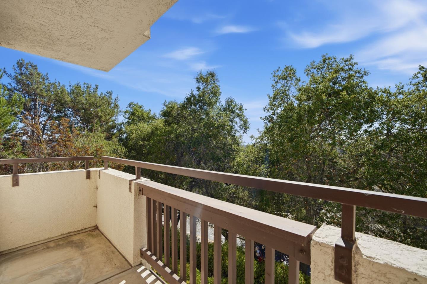Concrete balcony with brown railings overlooking leafy trees.