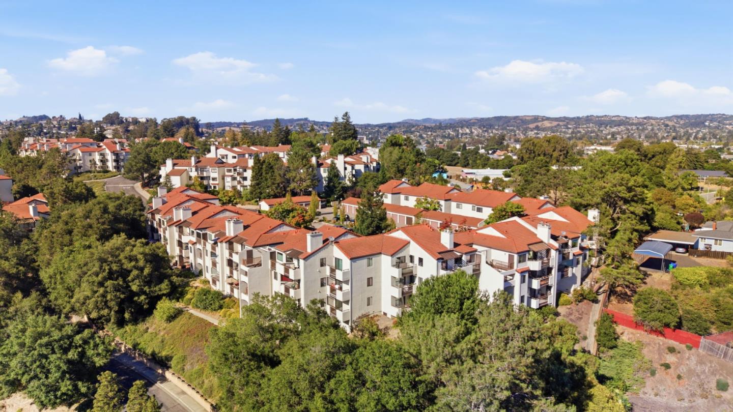 Aerial view of terracotta-roofed apartment buildings amid trees, with rolling hills in the distance.