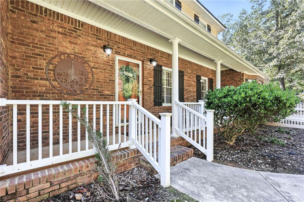 Brick home with a covered porch, white railings, black shutters, and a landscaped entry.