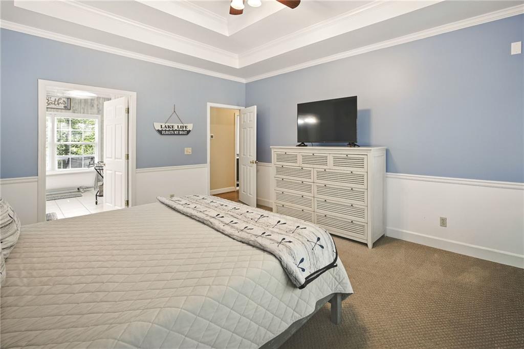 Bedroom with blue walls, white wainscoting, a tray ceiling, and a white dresser beneath a television.