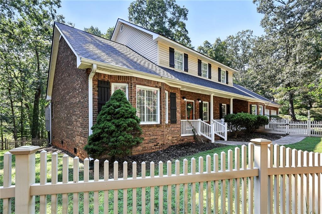 Two-story brick and siding home with a covered porch behind a white picket fence.
