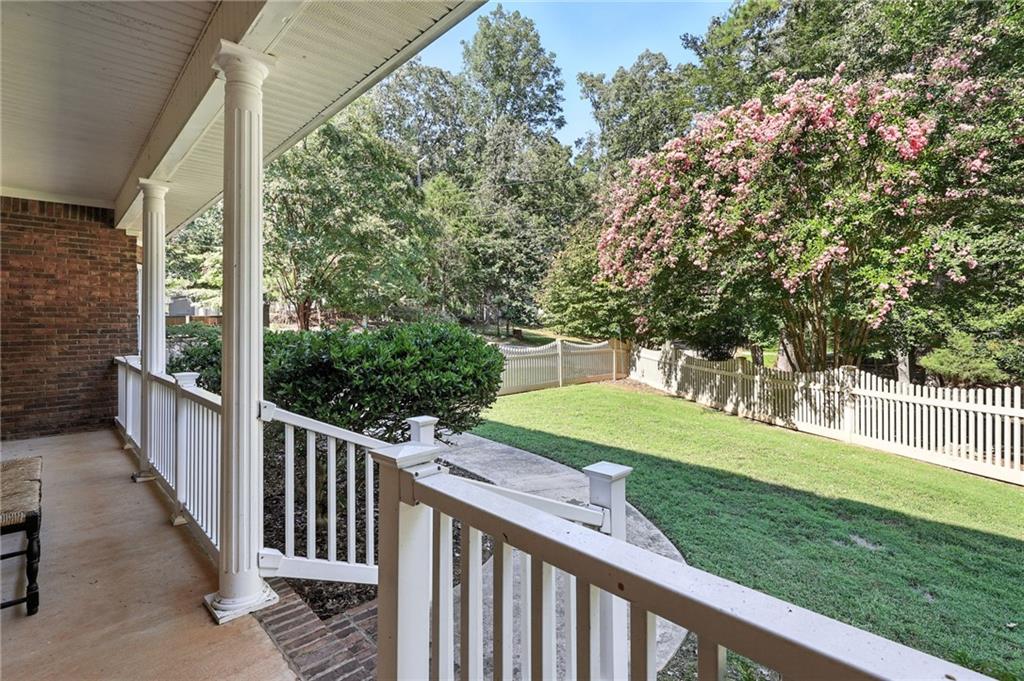 Covered porch overlooking a fenced lawn and flowering trees.
