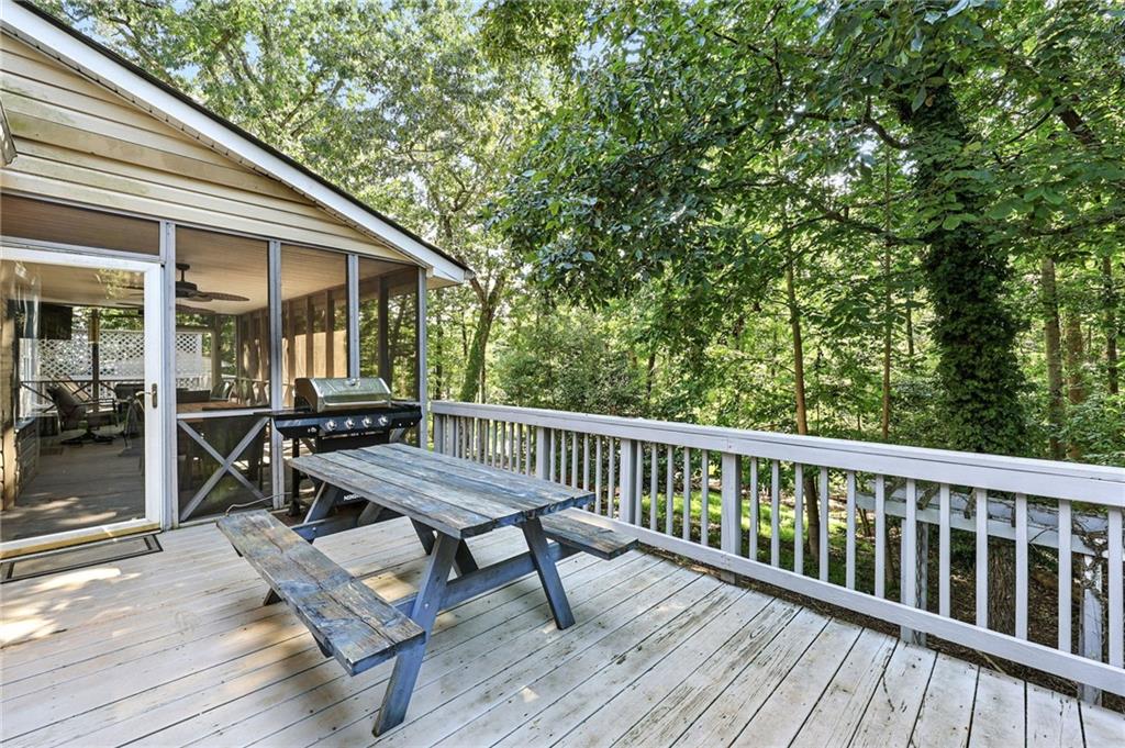 Wooden deck with picnic table and grill beside a screened porch, surrounded by trees.