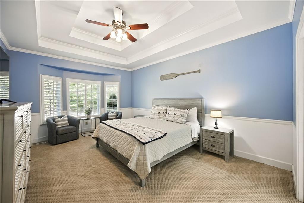 Blue bedroom with a tray ceiling, shuttered windows, and a bed between matching nightstands.