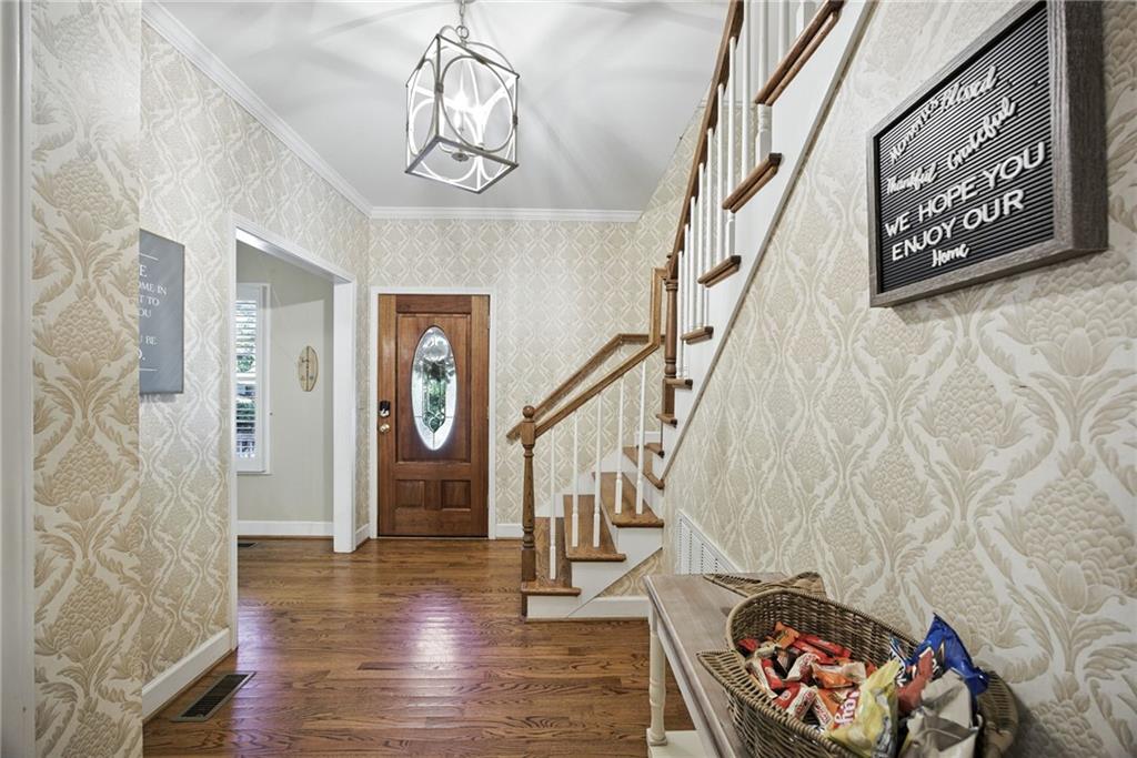 Entry foyer with patterned wallpaper, hardwood floors, a glass-paneled front door, and a staircase.