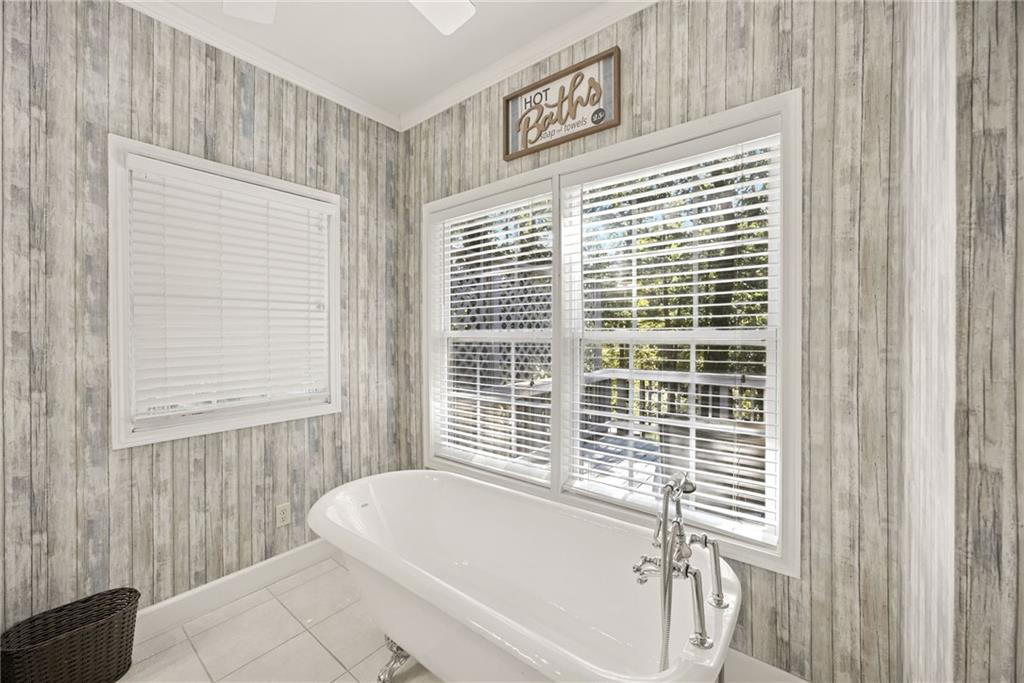 Bathroom with a white freestanding soaking tub beneath wide windows and weathered gray plank walls.